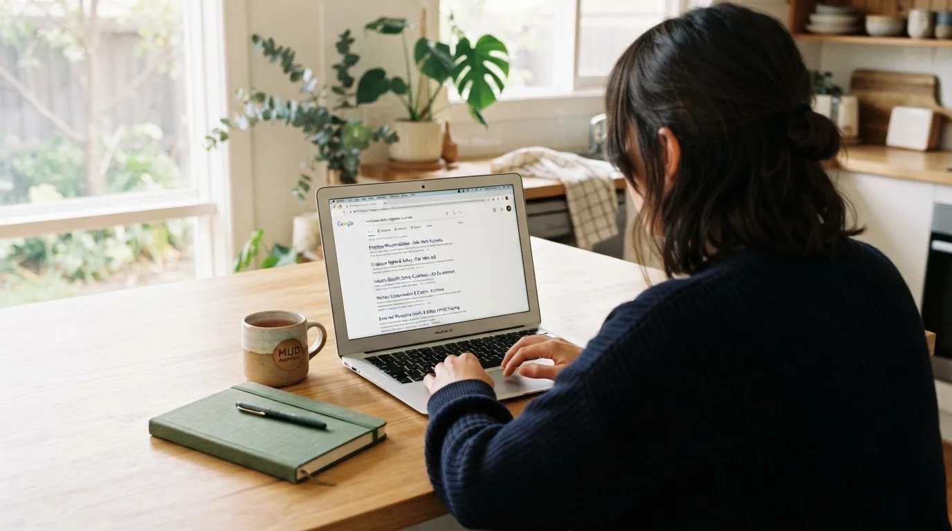 A person sits at a kitchen table, scrolling a laptop showing a general search results page about casino safety claims.
